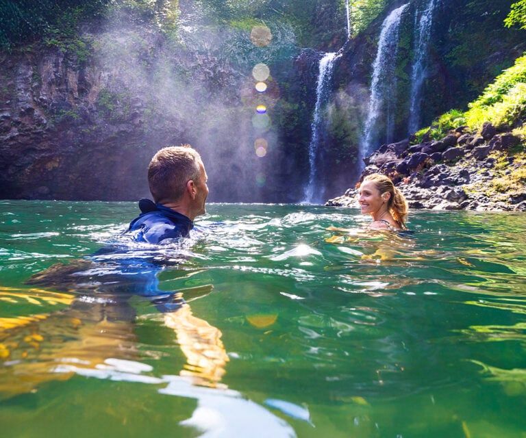 Couple swimming beneath a private waterfall on the hike & swim tour