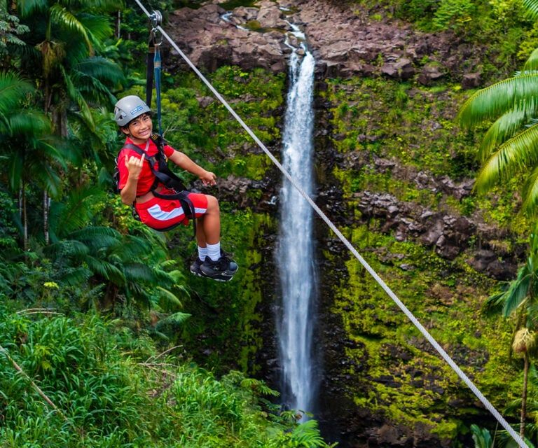 Child guest ziplining over Kolekole Falls waterfall